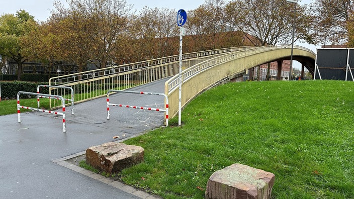 Zugang zur Fußgängerbrücke über die B1 mit rot-weißen Sperrbügeln und einem Fußgängerschild