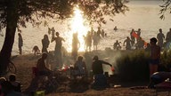 Viele Menschen sitzen am Masurenseeufer und einige schwimmen im See im Sonnenuntergang.