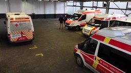 Zwei Meschen stehen zwischen Rettungswagen des Deutschen Roten Kreuzes in einer Halle