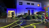 Die Feuerwehr vor dem Haus, im Vordergrund mehrere Schläuche und ein Feuerwehrauto