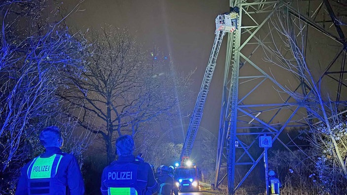 Im Dunkeln ist die Drehleiter der Feuerwehr zwölf Meter hoch ausgefahren, neben einem Strommast, im Vordergrund stehen zwei Polizisten