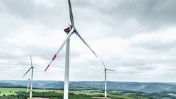 mehrere Windräder auf einer großen Fläche vor bewölktem Himmel