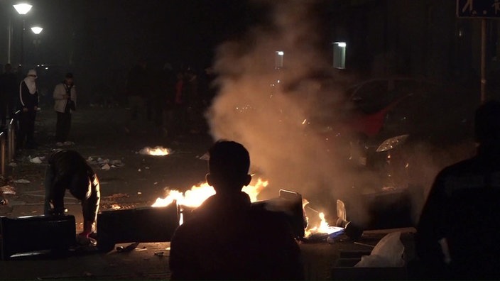 Schattenriss eines Kindes vor Feuer und Rauch, daneben eine gebückte Person