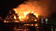 Ein großer Haufen brennender Heuballen, mehrere Feuerwehrleute sind zu sehen