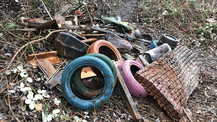 Am Ufer eines Baches liegen gesammelter Sperrmüll und Schrott.