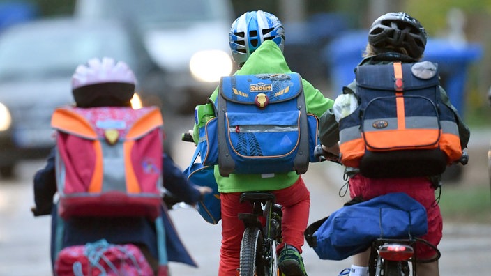 Drei Kinder fahren mit einem Fahrrad über die Straße.