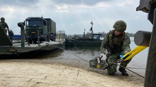 Soldaten bei der Übung am Steg, mehrere Militärfahrzeuge stehen im Hintergrund.