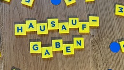 Mit bunten Buchstaben steht "Hausaufgaben" auf einem Tisch.