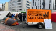 Ein Protestcamp samt Zelten und Anhängern ist in einer Innenstadt aufgebaut.