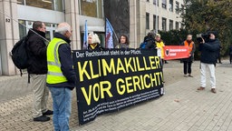 Demonstrierende vor dem Landgericht Essen halten ein Banner mit dem Schriftzug "Klimakiller vor Gericht"