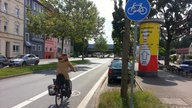 Radfahrerin radelt auf dem eingezeichneten Radweg an der Seite einer größeren Straße