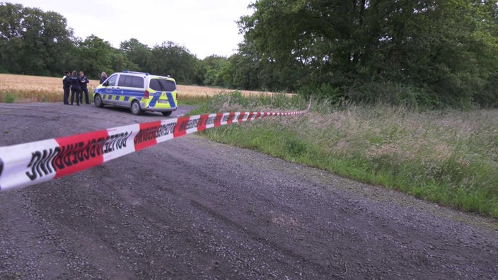 Ein Polizeiauto steht hinter einer Absperrung in einem Waldgebiets