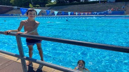 Kleiner Junge am Beckenrand und ein Mädchen im Wasser 