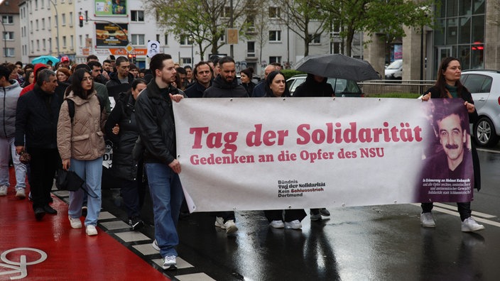 Der Schweigemarsch mit 300 Menschen, davor ein Banner: "Tag der Solidarität - Gedenken an die Opfer des NSU" und ein Bild von Mehmet Kubaşık 