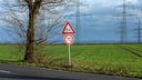 Zwei Verkehrsschilder an einer Landstraße: Ein Tempo-70-Schild unter einem "Achtung, Radfahrer"-Schild. Dahinter sind Strommasten zu sehen.