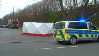 Ein Polizeiauto steht vor einem Sichtschutz an einer Unfallstelle, im Hintergrund steht ein Lkw