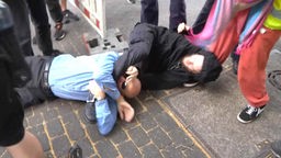Ein Mann liegt auf dem Boden und beißt einem Demonstranten in die Wade