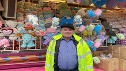 Ein Mann mit gleber Jacke steht vor Kuscheltieren am Losstand