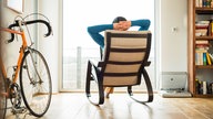 junger Mann im Schaukelstuhl, Rennrad im Zimmer 