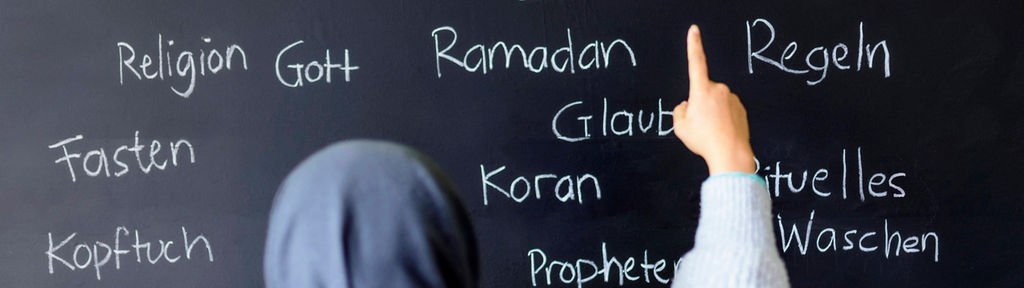 Eine muslimische Schülerin vor einer Tafel mit Begriffen aus dem Islam im Islamunterricht