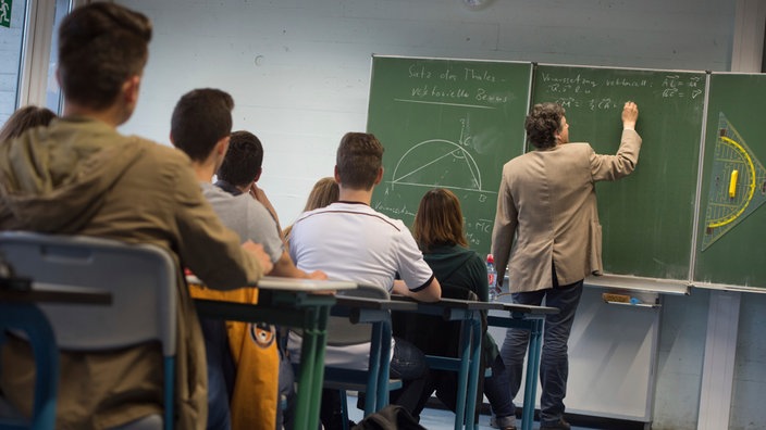 Symbolbild: Ein Lehrer schreibt während des Matheunterrichts einer Abiturklasse an die Tafel.