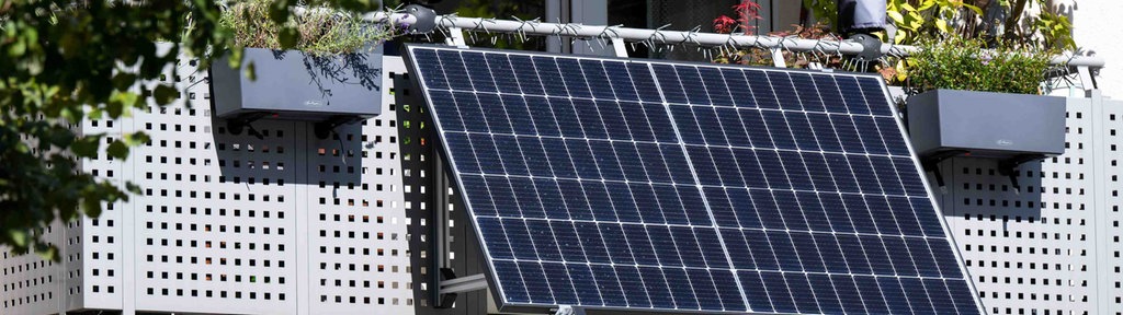 Zu sehen ist ein Balkon mit Pflanzen. Am Balkon befestigt ist eine Solaranlage.