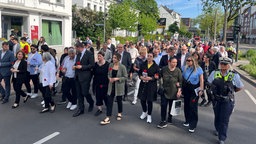 Viele Menschen laufen geschlossen eine Straße entlang. In den Händen halten sie Blumen.