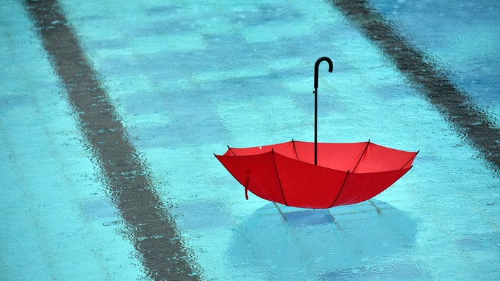 Bei Regen schwimmt ein Regenschirm im Freibad