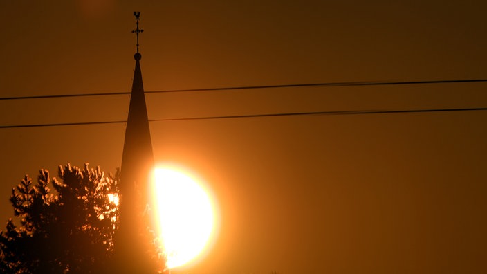 Die Sonne geht hinter der Kirche von Roggendorf bei Köln auf.