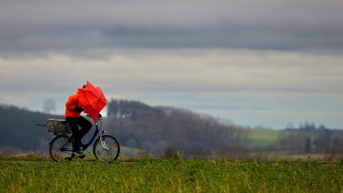 Ein Radfahrer ist bei Regen und Sturm mit einem Regenschirm unterwegs