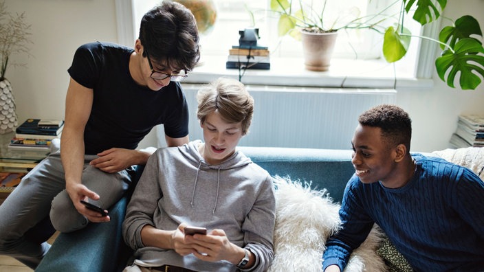 Jugendliche sitzen auf dem Sofa und nutzen Handys 