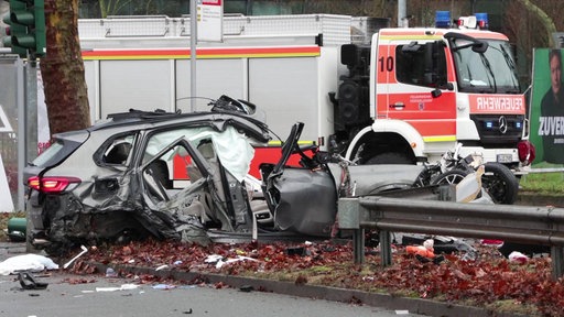 Ein zerstörtes Auto. Im Hintergrund ein Feuerwehrwagen