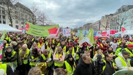 Viele Menschen in gelben Warnwesten und großen Transparenten versammelt auf einem großen Platz