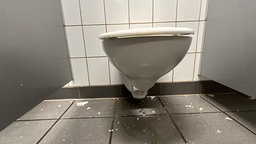 Um eine kaputte Toilettenschüssel liegen zahlreiche Keramiksplitter.