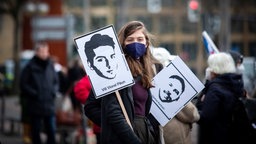 Pressefoto "Demo", bei dem eine Frau mit zwei Plakaten zur Kamera schaut