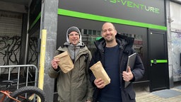 Lukas und Jos stehen mit zwei Tüten vor dem Cannabis Ladengeschäft