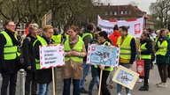 Demonstrierende mit Warnwesten und Plakaten.