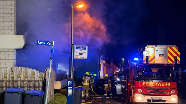 ein Feuerwehrauto mit Feuerwehrleuten vor einem rauchenden Haus