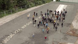 Mehrere Menschen auf einer Freifläche, auf der der Schriftzug "Wir sind das Volk. Wir sind ein Volk" steht.