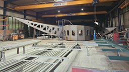 Eine riesige Stahlkonstruktion steht in einer Werkshalle.