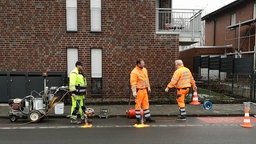 Es sind zu sehen 3 Bauarbeiter, die die Straße abflemmen