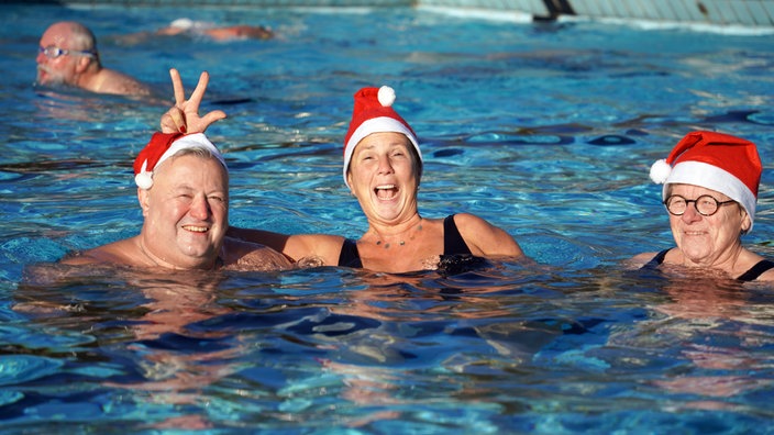 Mehrere Menschen sind in einem Schwimmbecken und tragen weihnachtliche Mützen.