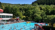 Das Schwimmbecken des Freibades in Netphen, der Himmel ist blau, im Hintergrund sind Wälder zu sehen