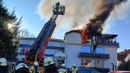 Flammen schlagen aus Dachgeschosswohnung, Feuerwehr mit Drehkran im Einsatz