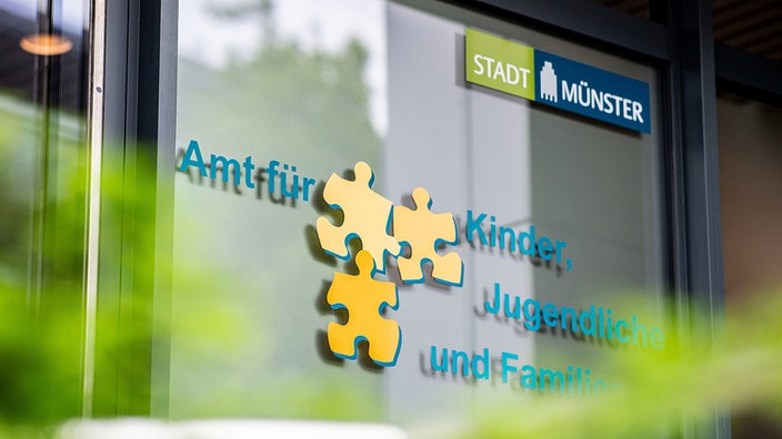 Die Eingangstür des Jugendamts in Münster. Darauf steht "Amt für Kinder, Jugendliche und Familie" dazwischen drei Puzzleteile.