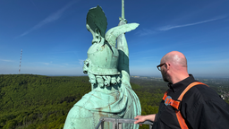 Ein Mann begutachtet das Herrmannsdenkmal, er steht dabei auf einem Gerüst.