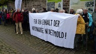 Eine Gruppe von Menschen hält ein Banner hoch, mit der Aufschrift "Für den Erhalt der Hofynagoge in Detmold!"