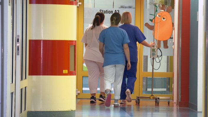 Drei Krankenschwestern laufen den Flur entlang in der Klinik. 