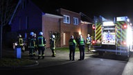 Feuerwehrmänner und ein Feuerwehrauto vor einem Wohnhaus stehend. 