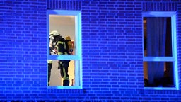 Ein Feuerwehrmann ist von außen hinter einem Fenster des Wohnhauses zu sehen. 